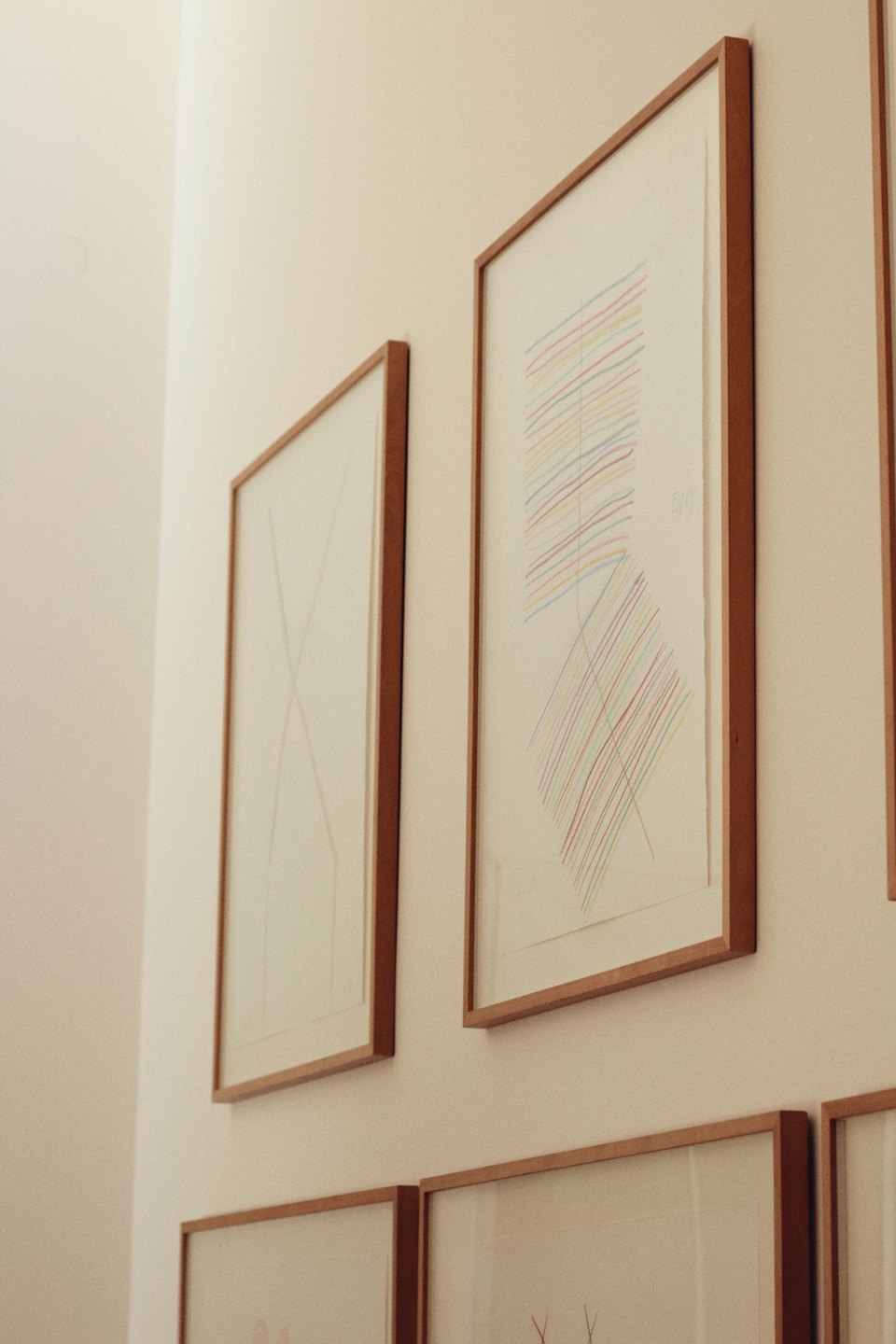 Dwa oprawione abstrakcyjne obrazy wiszą na beżowej ścianie galerii.
